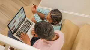 A man and a child sit on stairs, focused on a laptop, sharing a moment of learning and technology together.