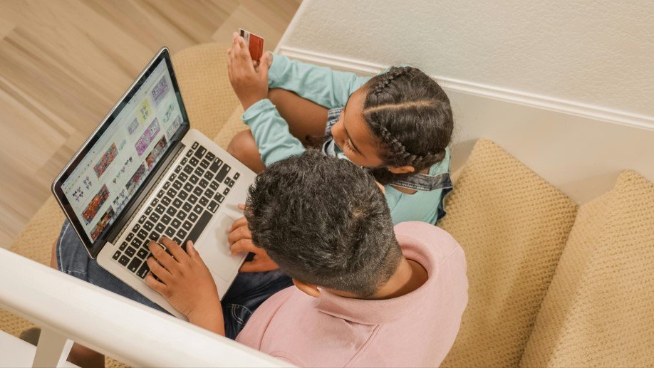 A man and a child sit on stairs, focused on a laptop, sharing a moment of learning and technology together.